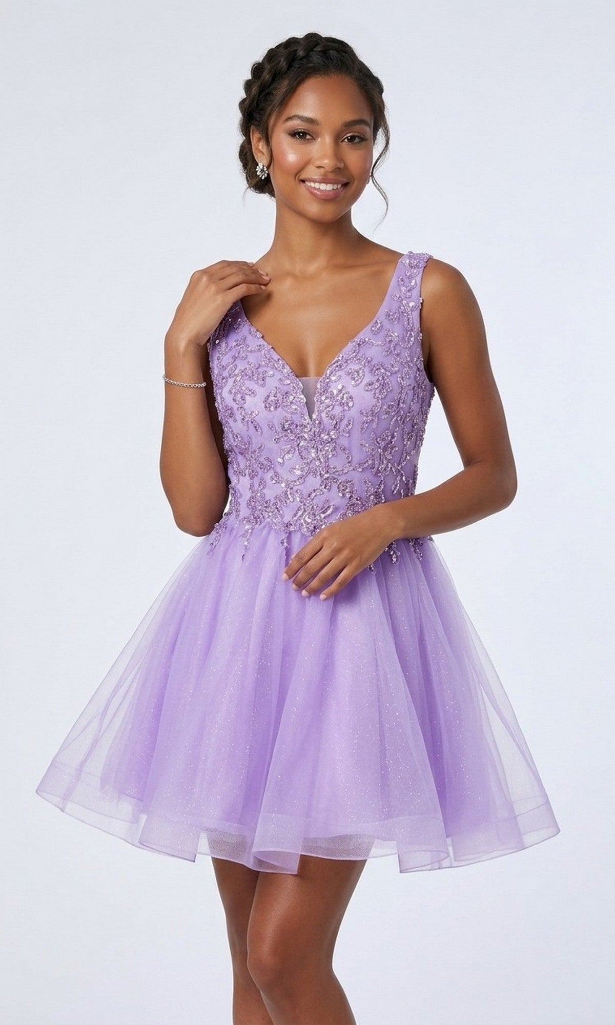 A woman poses against a plain background wearing the Chicas C376 short homecoming dress in lilac—a sleeveless, knee-length design with floral embellishments and a glitter tulle skirt, showcasing a classic fit-and-flare silhouette.
